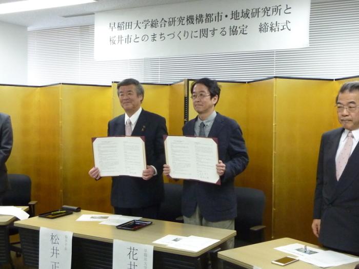 協定書を掲げる松井市長（左）と花井機構長（右）