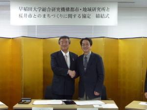 握手を交わす松井市長（左）と花井機構長（右）